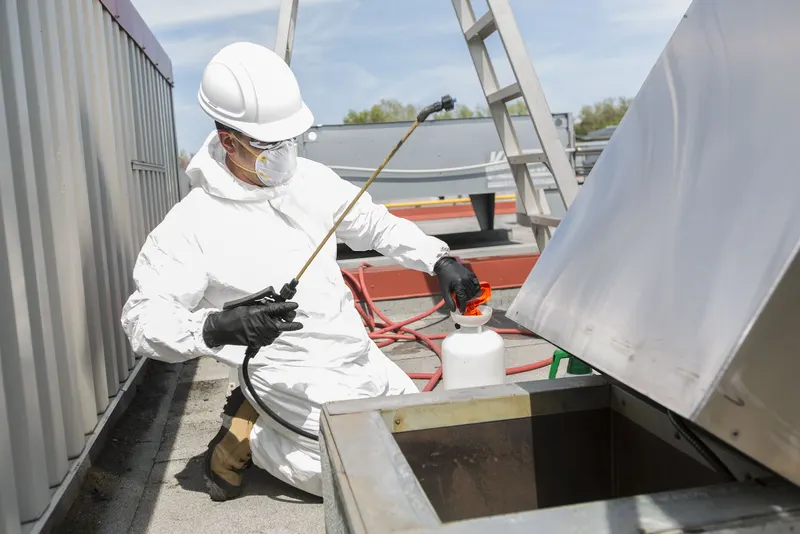 Rooftop exhaust fan tipped back on its hinge while a technician cleans inside the housing