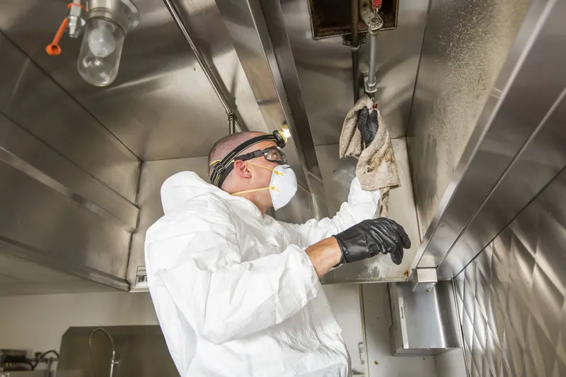 Technician wiping the plenum ledge inside an exhaust hood beside the suppression nozzle piping